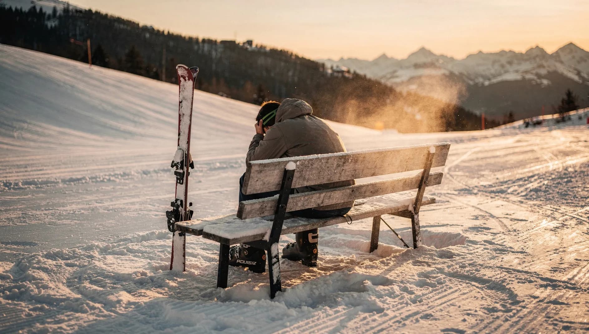Skifahrer macht Pause auf einer Bank am Pistenrand